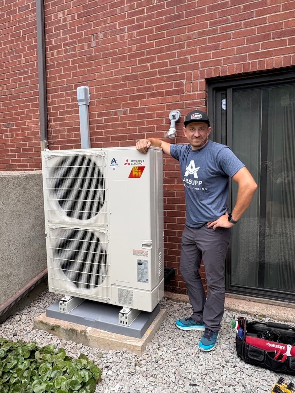 AirSupp's owner beside a newly installed Mitsubishi Electric heat pump outdoor unit on a concrete pad