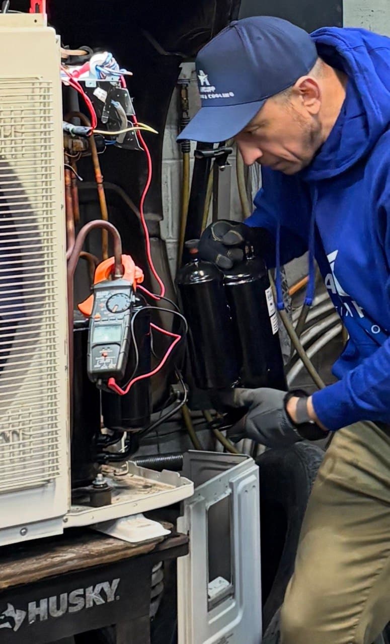 Testing a heat pump outdoor unit's wiring with a clamp meter during a repair visit